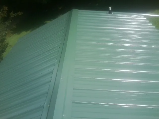 New green metal panels meeting at the ridge of a roof — Flat Roof Repair work by our crew in Anna