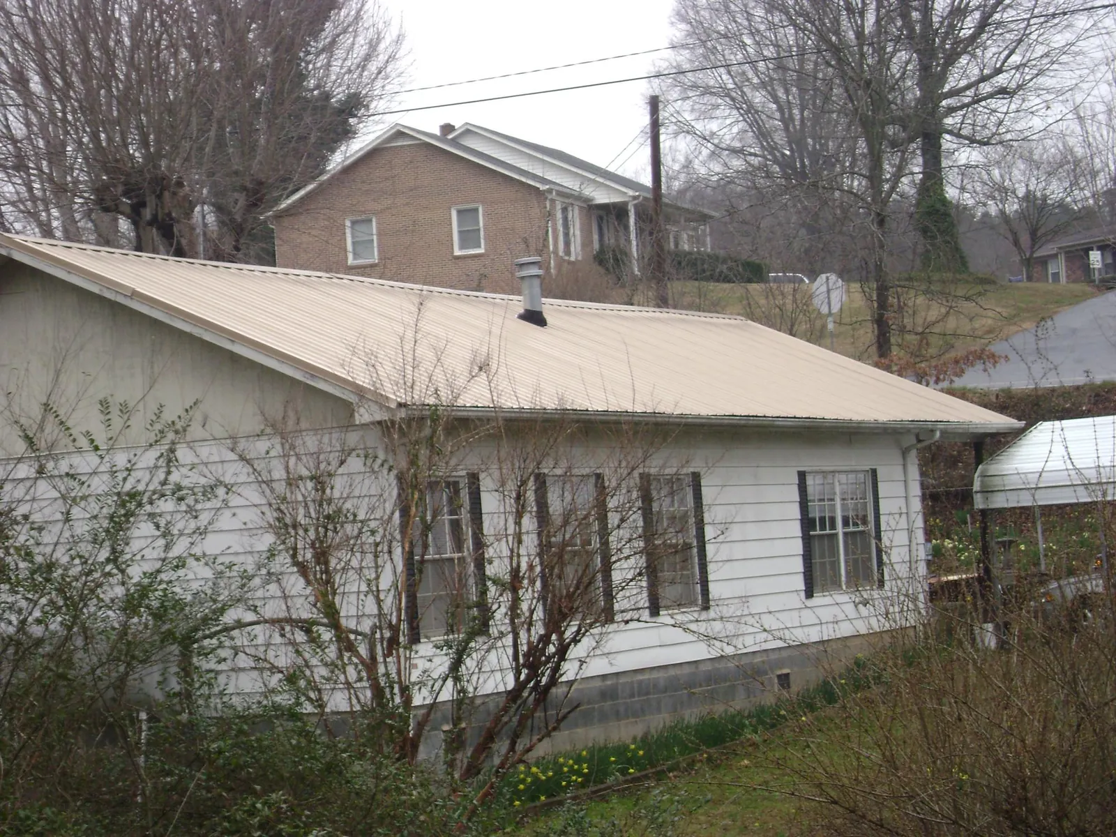 Tan metal roof on a white sided house set into a hillside — Commercial Roofing by Roofing Brothers in Anna